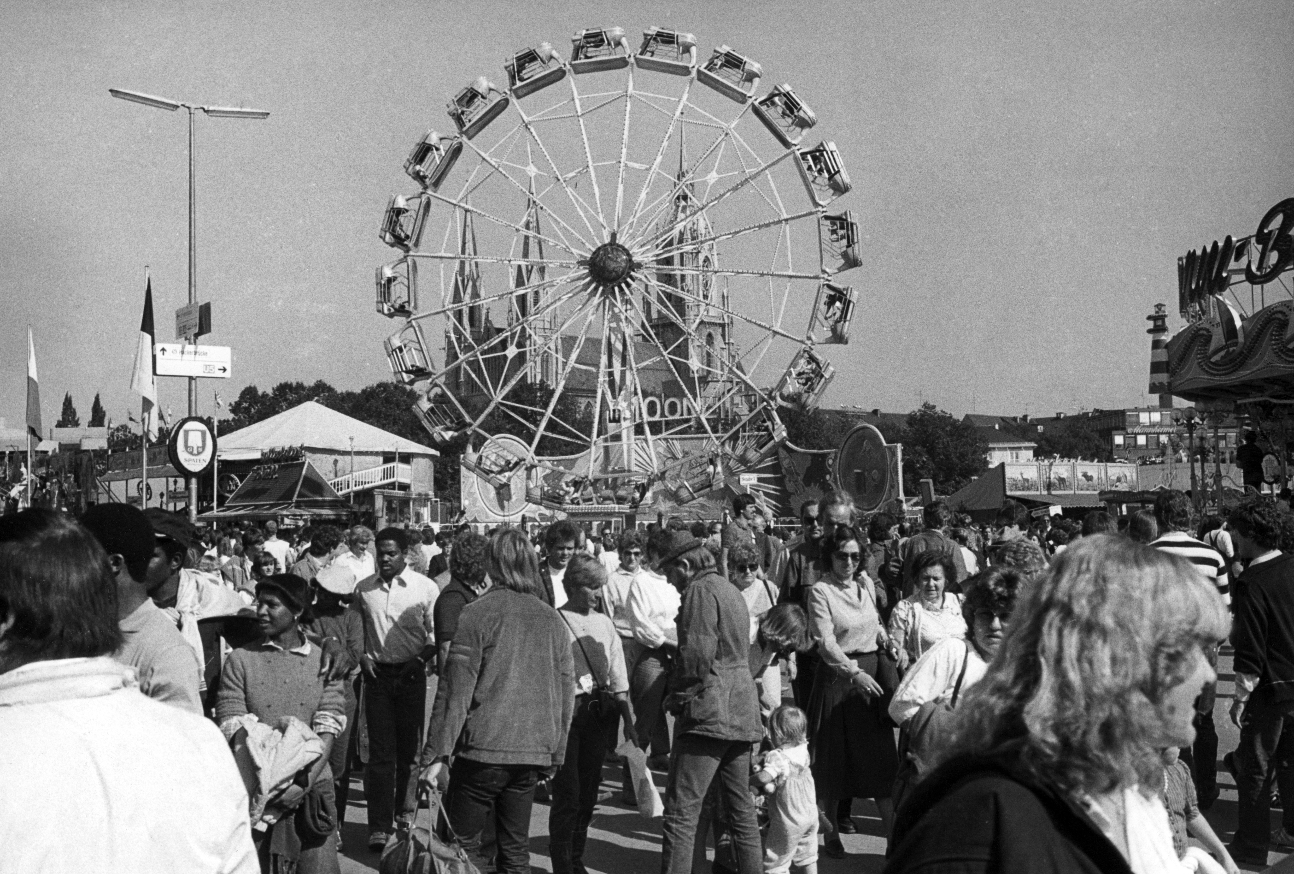 


                 Viele verschiedene Personen auf dem Oktoberfest mit einem Riesenrad und der Pauls Kirche im Hintergrund.